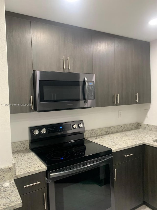 kitchen with light stone countertops, appliances with stainless steel finishes, and dark brown cabinetry