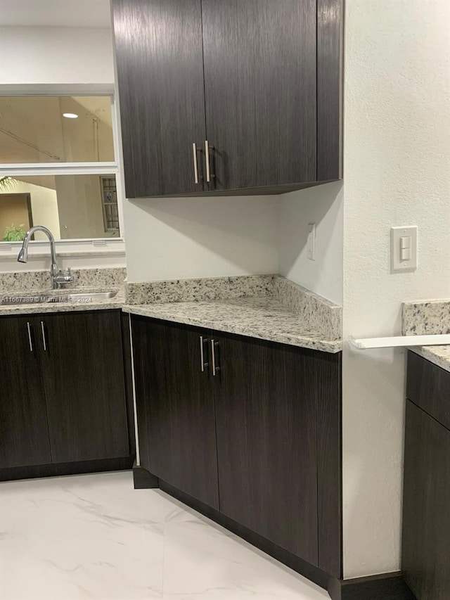 kitchen featuring light stone counters, dark brown cabinetry, and sink