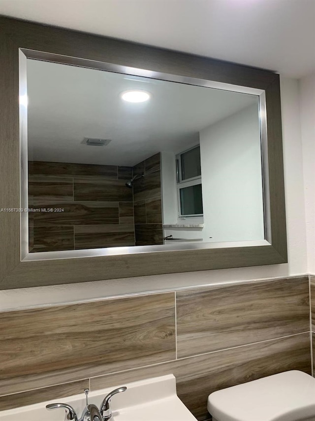 bathroom with tiled shower, toilet, and sink