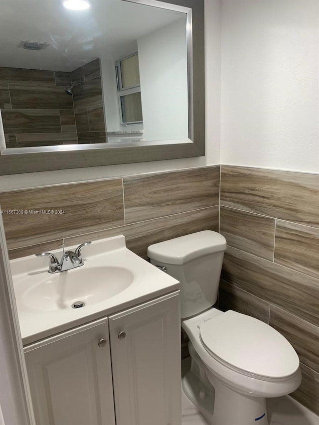 bathroom with tile walls, walk in shower, vanity, and toilet