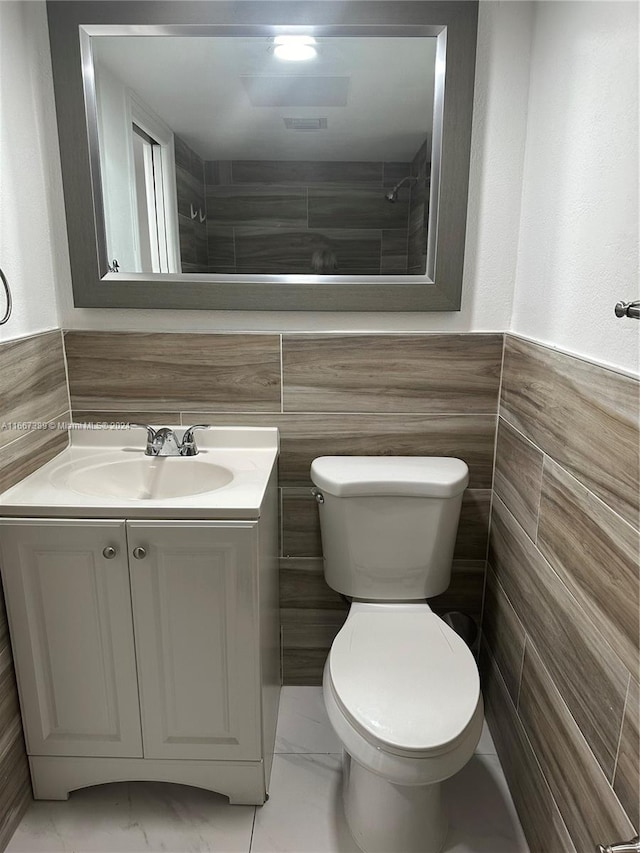 bathroom featuring tile walls, a tile shower, vanity, and toilet