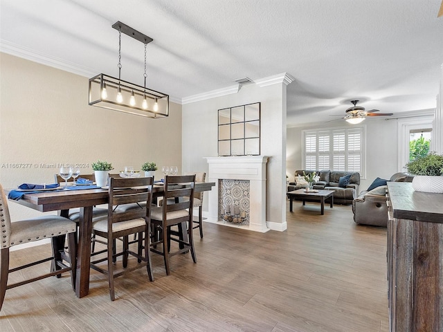 dining room featuring wood-type flooring, ceiling fan, a textured ceiling, and crown molding