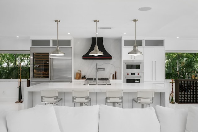 kitchen with a breakfast bar, hanging light fixtures, a healthy amount of sunlight, and premium range hood