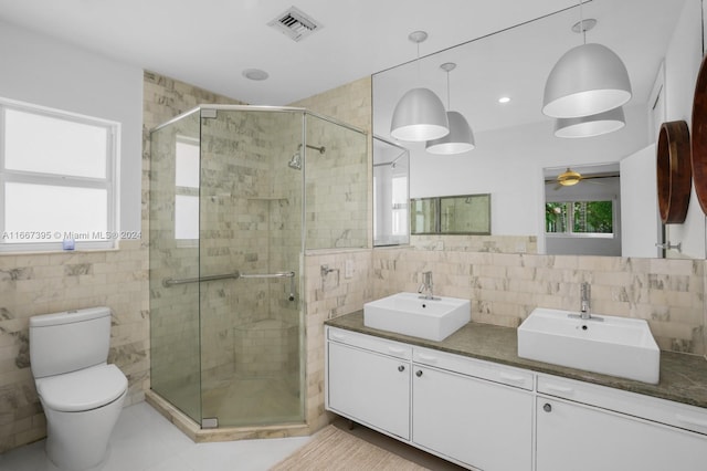 bathroom with tile walls, a shower with door, vanity, and toilet