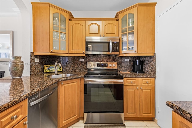 kitchen with dark stone countertops, tasteful backsplash, light tile patterned floors, stainless steel appliances, and sink