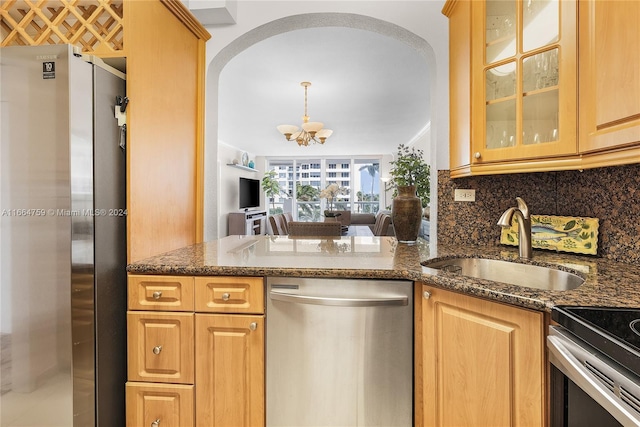 kitchen with backsplash, stainless steel appliances, dark stone counters, sink, and a notable chandelier