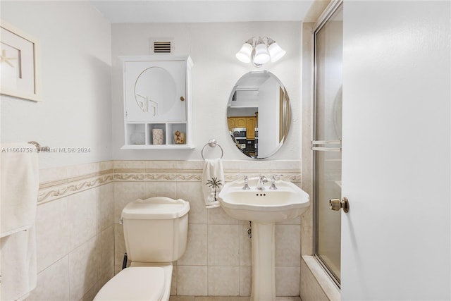 bathroom featuring tile walls, shower / bath combination with glass door, and toilet