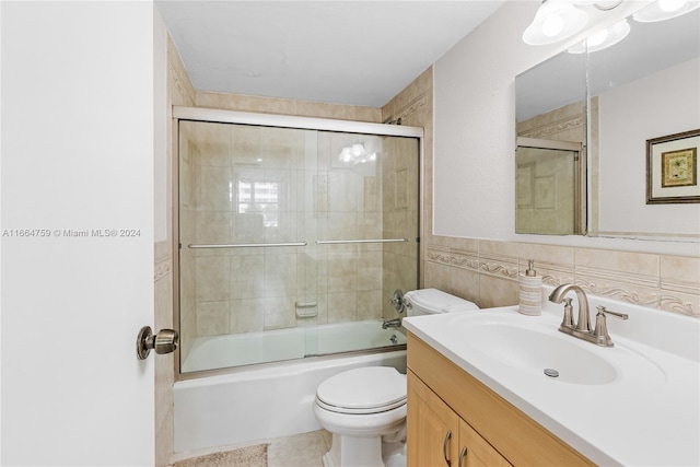 full bathroom with shower / bath combination with glass door, tile walls, vanity, and toilet