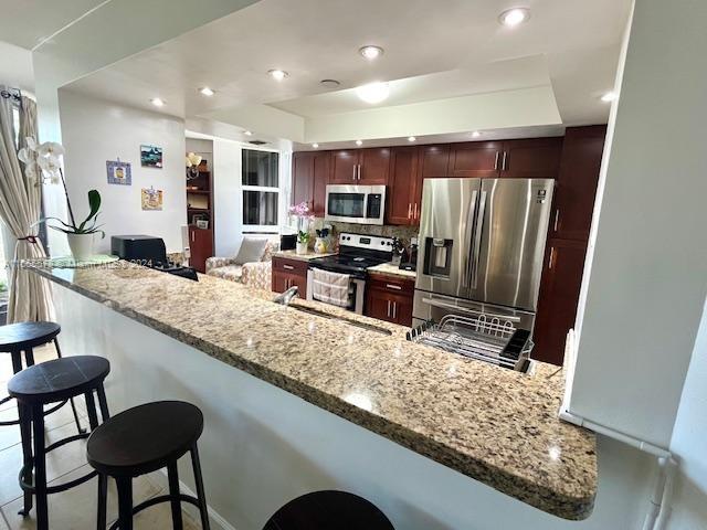 kitchen featuring light stone countertops, a kitchen bar, kitchen peninsula, and appliances with stainless steel finishes