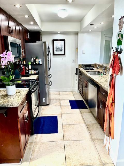 kitchen with light tile patterned floors, light stone countertops, stainless steel appliances, and sink