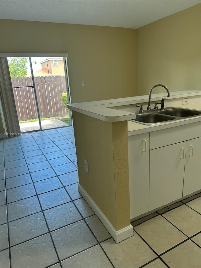 kitchen with light tile patterned flooring, kitchen peninsula, and sink