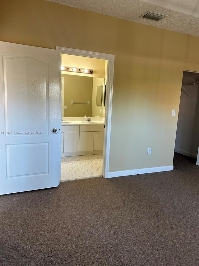 unfurnished bedroom featuring connected bathroom, carpet, a textured ceiling, and sink