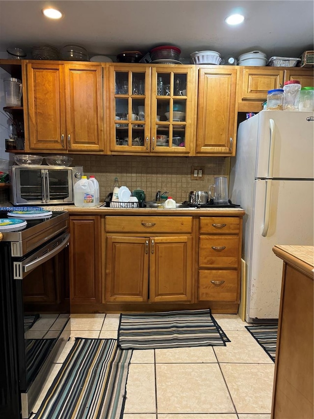 kitchen featuring white refrigerator, stove, light tile patterned floors, tile countertops, and decorative backsplash