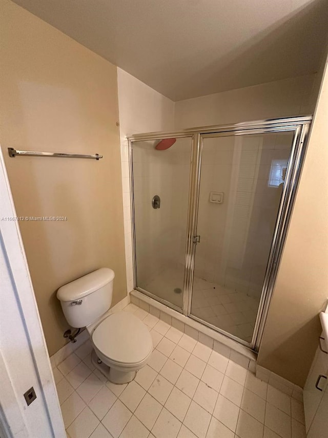 bathroom featuring tile patterned flooring, a shower with shower door, and toilet