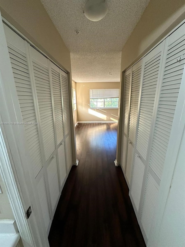 corridor with a textured ceiling and dark hardwood / wood-style flooring