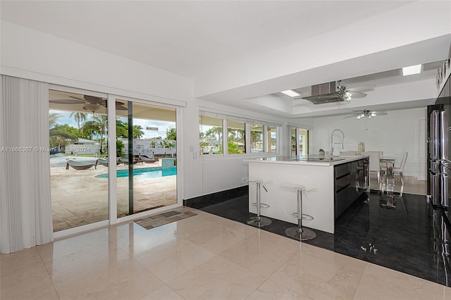 kitchen featuring ceiling fan, an island with sink, a kitchen breakfast bar, and a healthy amount of sunlight