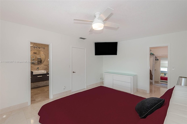 bedroom with sink, a walk in closet, ensuite bathroom, light tile patterned floors, and ceiling fan