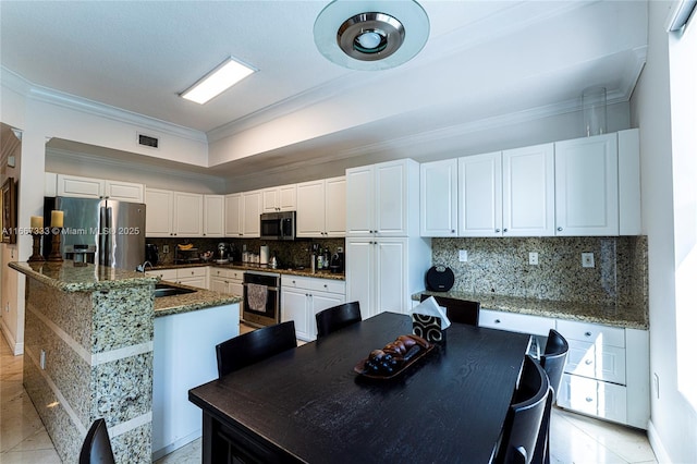 kitchen with white cabinets, appliances with stainless steel finishes, a center island with sink, and dark stone counters