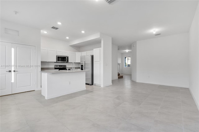 kitchen featuring stainless steel appliances, sink, light tile patterned floors, white cabinetry, and an island with sink