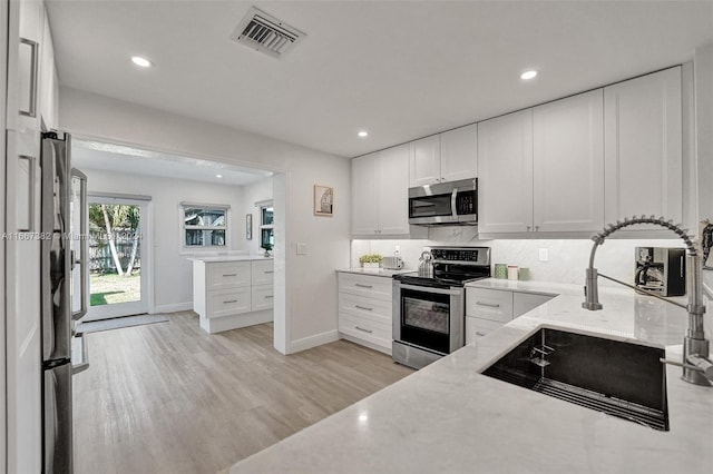 kitchen featuring white cabinets, sink, appliances with stainless steel finishes, light hardwood / wood-style floors, and light stone counters