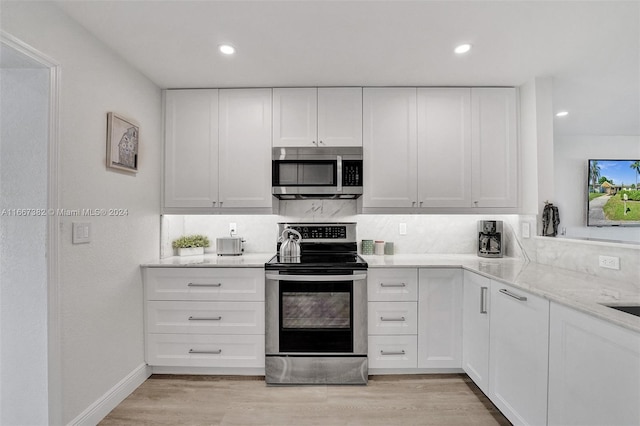 kitchen featuring stainless steel appliances, light stone counters, decorative backsplash, white cabinets, and light wood-type flooring