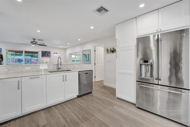 kitchen featuring white cabinets, sink, light stone countertops, light wood-type flooring, and stainless steel appliances