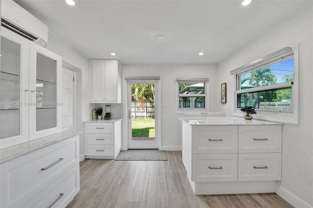 kitchen featuring white cabinets, light stone countertops, an AC wall unit, and light hardwood / wood-style flooring