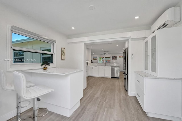 kitchen with a kitchen bar, kitchen peninsula, stainless steel appliances, light hardwood / wood-style flooring, and white cabinetry