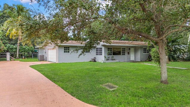view of front facade with central air condition unit, stucco siding, driveway, an attached garage, and a front lawn