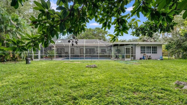 back of property with a lanai, an outdoor pool, and a yard