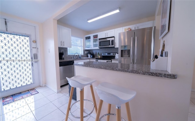 kitchen with backsplash, white cabinetry, stainless steel appliances, a kitchen breakfast bar, and dark stone counters