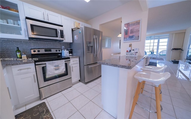 kitchen with stainless steel appliances, white cabinets, dark stone countertops, and a breakfast bar area