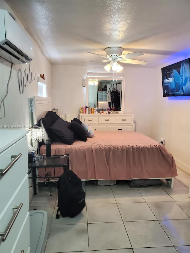 bedroom with a wall unit AC, ceiling fan, light tile patterned floors, and a textured ceiling