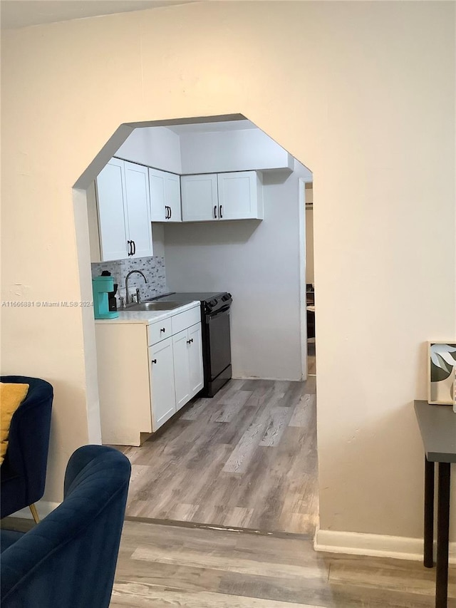 kitchen with white cabinets, sink, light hardwood / wood-style flooring, backsplash, and black dishwasher