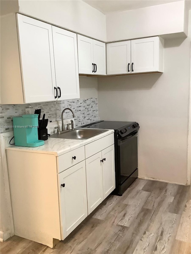 kitchen with black range with electric stovetop, white cabinets, sink, backsplash, and light hardwood / wood-style floors