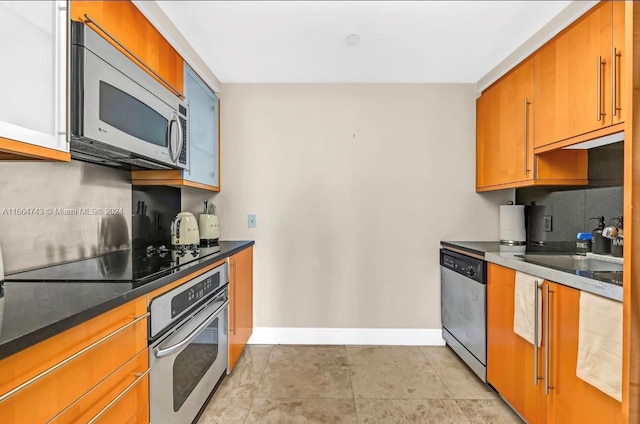 kitchen featuring dark countertops, a sink, brown cabinets, stainless steel appliances, and baseboards