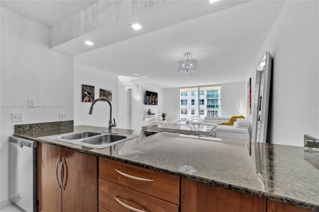 kitchen with dark stone counters, stainless steel dishwasher, sink, and a chandelier