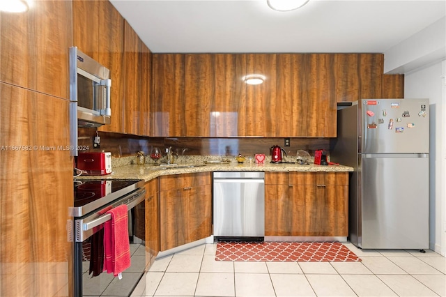 kitchen with light stone countertops, sink, stainless steel appliances, wooden walls, and light tile patterned floors