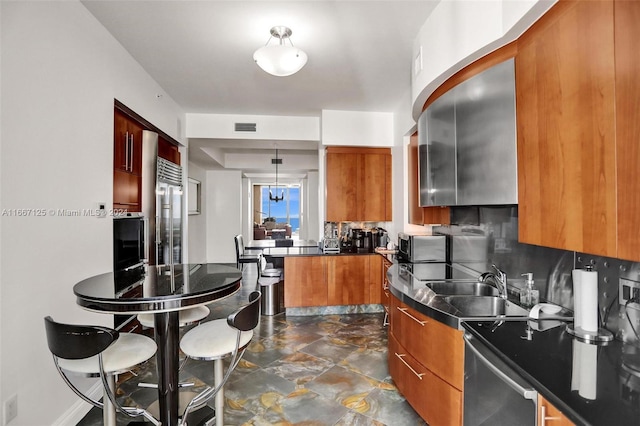 kitchen featuring brown cabinets, stainless steel built in refrigerator, dark countertops, a sink, and a peninsula