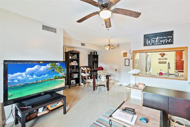 living room with a textured ceiling, ceiling fan with notable chandelier, and light tile patterned flooring