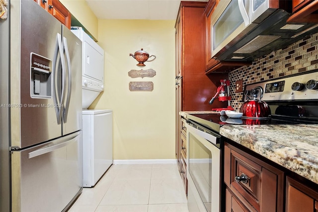 kitchen with light stone countertops, stainless steel appliances, backsplash, and stacked washer / drying machine