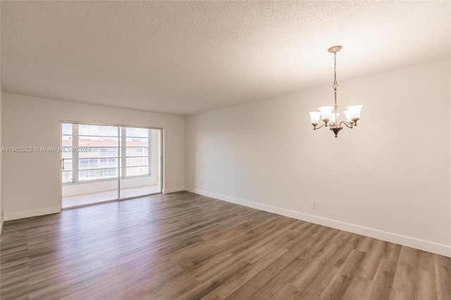 empty room featuring hardwood / wood-style flooring, a chandelier, and a textured ceiling