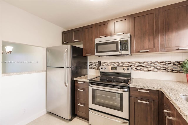 kitchen featuring light stone counters, dark brown cabinets, stainless steel appliances, and tasteful backsplash