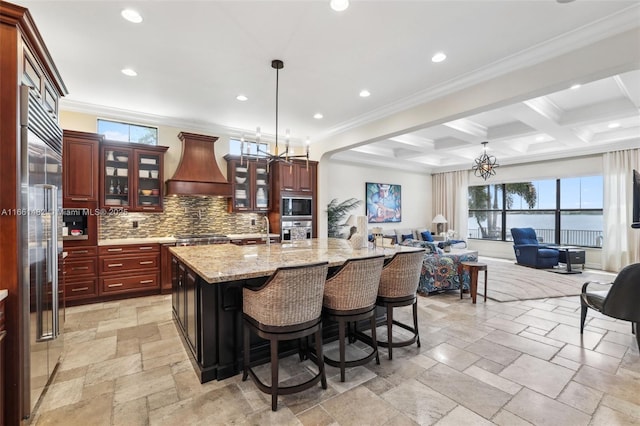 kitchen featuring beamed ceiling, premium range hood, coffered ceiling, a kitchen island with sink, and stainless steel appliances