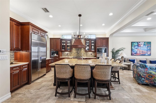 kitchen with crown molding, a spacious island, premium range hood, a breakfast bar area, and built in appliances