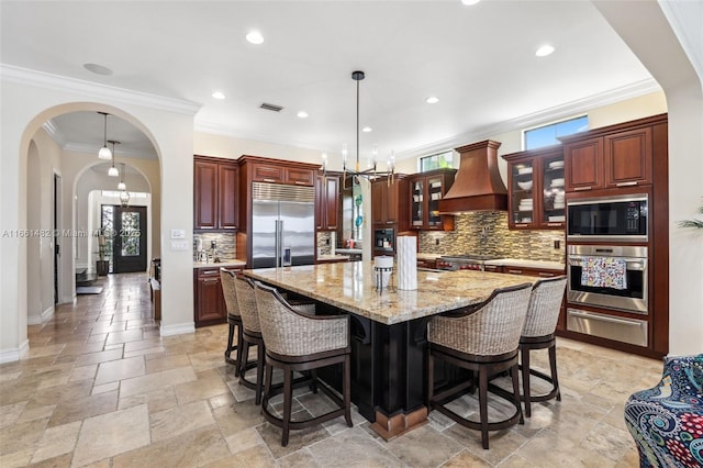 kitchen featuring premium range hood, hanging light fixtures, a kitchen breakfast bar, a spacious island, and built in appliances