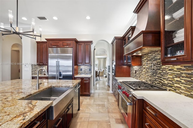 kitchen with premium appliances, decorative light fixtures, tasteful backsplash, light stone counters, and custom range hood