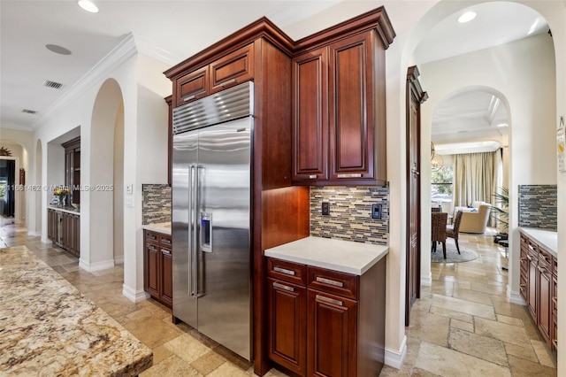 kitchen with stainless steel built in fridge, tasteful backsplash, light stone countertops, and ornamental molding