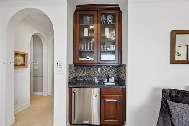 bar with light carpet, dark stone counters, backsplash, ornamental molding, and stainless steel refrigerator