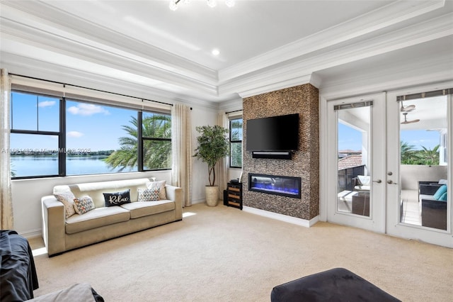 carpeted living room featuring a large fireplace, a tray ceiling, ornamental molding, and french doors